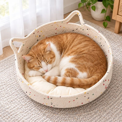 Chat roux et blanc endormi dans un panier pour chat en rotin avec coussin blanc près d’une fenêtre